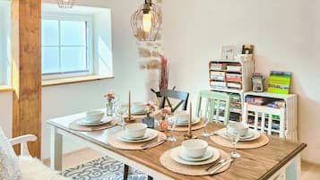 Un coin repas avec une table en bois dressée pour quatre personnes, entourée de chaises, avec une bibliothèque et une fenêtre en arrière-plan.
