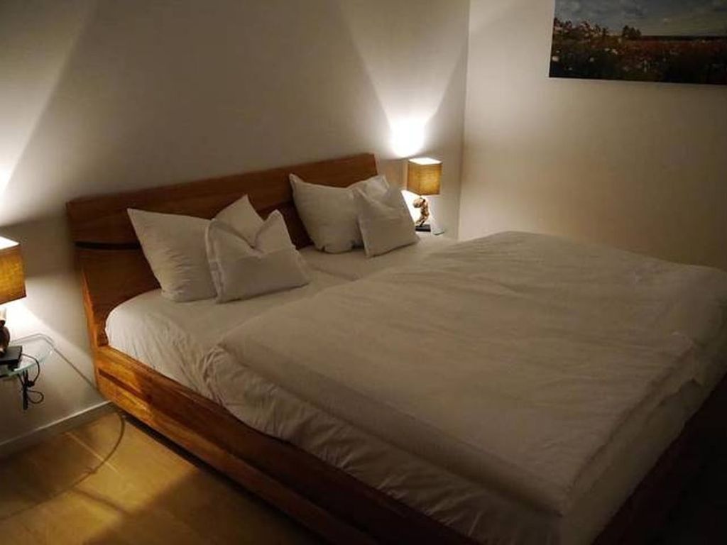 Ein ordentlich bezogenes Bett mit weißen Leinen und einem hölzernen Kopfteil in einem schlicht und modern eingerichteten Zimmer.