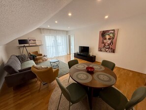 Un salon avec un canapé, un téléviseur, un tableau et une table à manger avec des chaises.