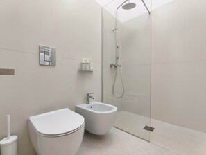 Et moderne badeværelse med toilet, bidet og bruseområde med glasvægge.