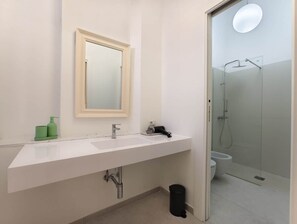 Et badeværelse med hvid vask, spejl og glasbrusekabine.