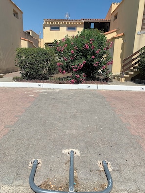 A paved area with a metal structure, adjacent to a building with a tiled roof and a pink flowering bush. - New Listing (Le Barcarès)