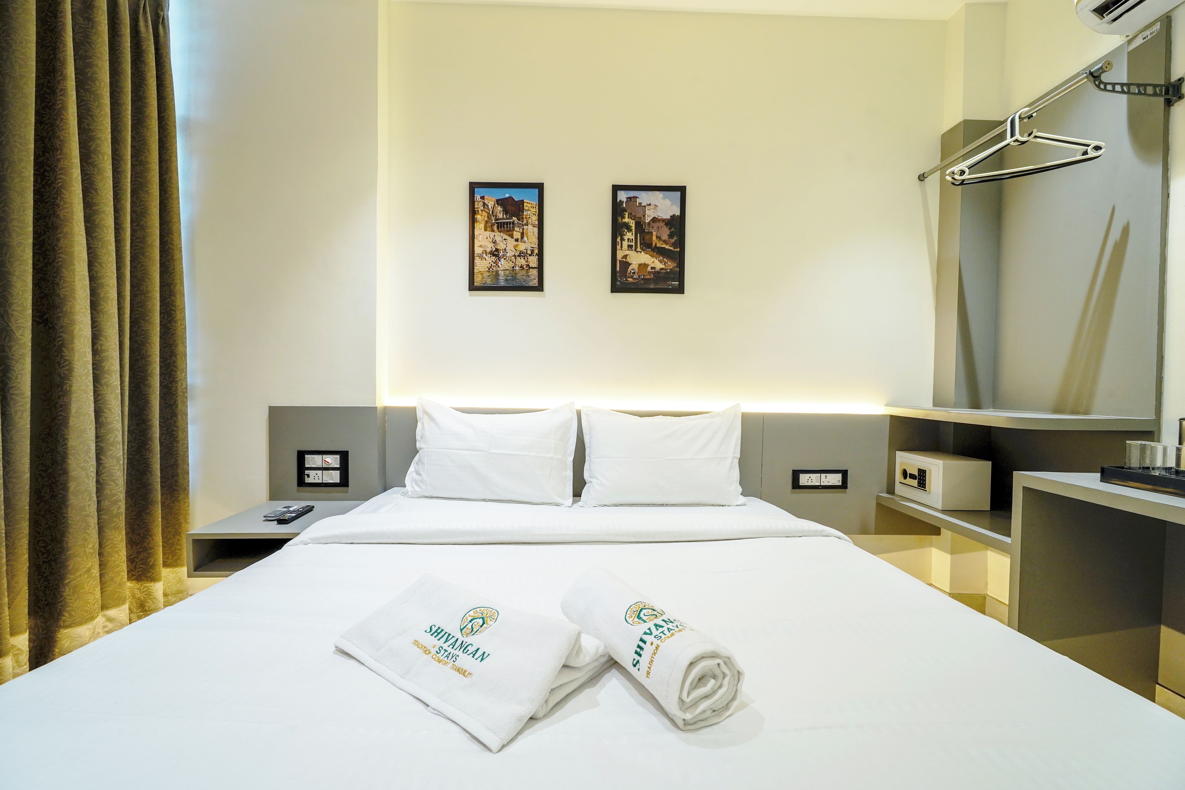 Una habitación de hotel con cama, dos almohadas, una mesita de noche, un espejo, una toalla y dos cuadros en la pared.
