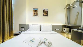 Una habitación de hotel con cama, dos almohadas, una mesita de noche, un espejo, una toalla y dos cuadros en la pared.