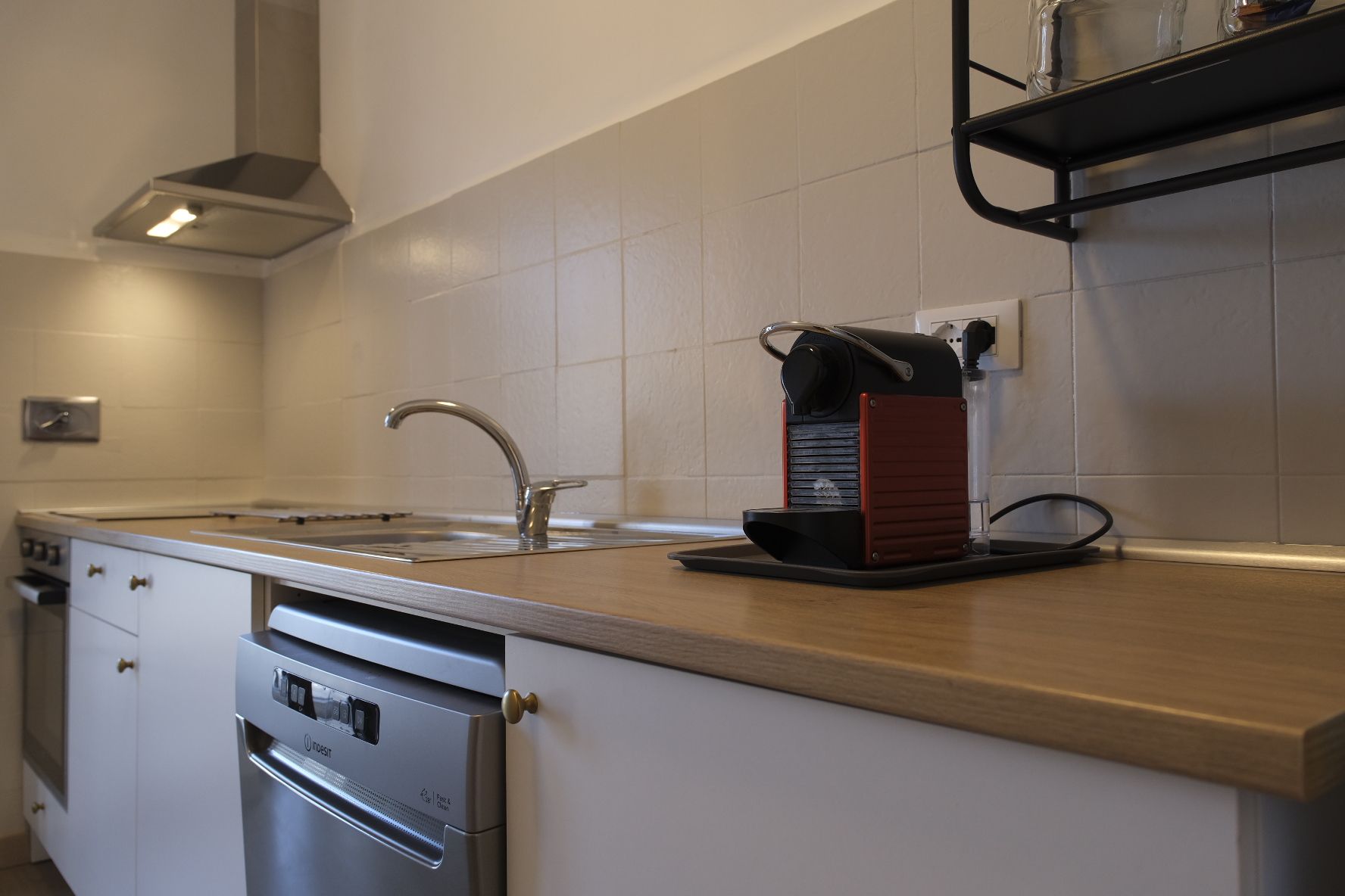 Ett kök med en diskmaskin i rostfritt stål, en kaffemaskin, en diskho med en modern blandare och en bänkskiva i trä.