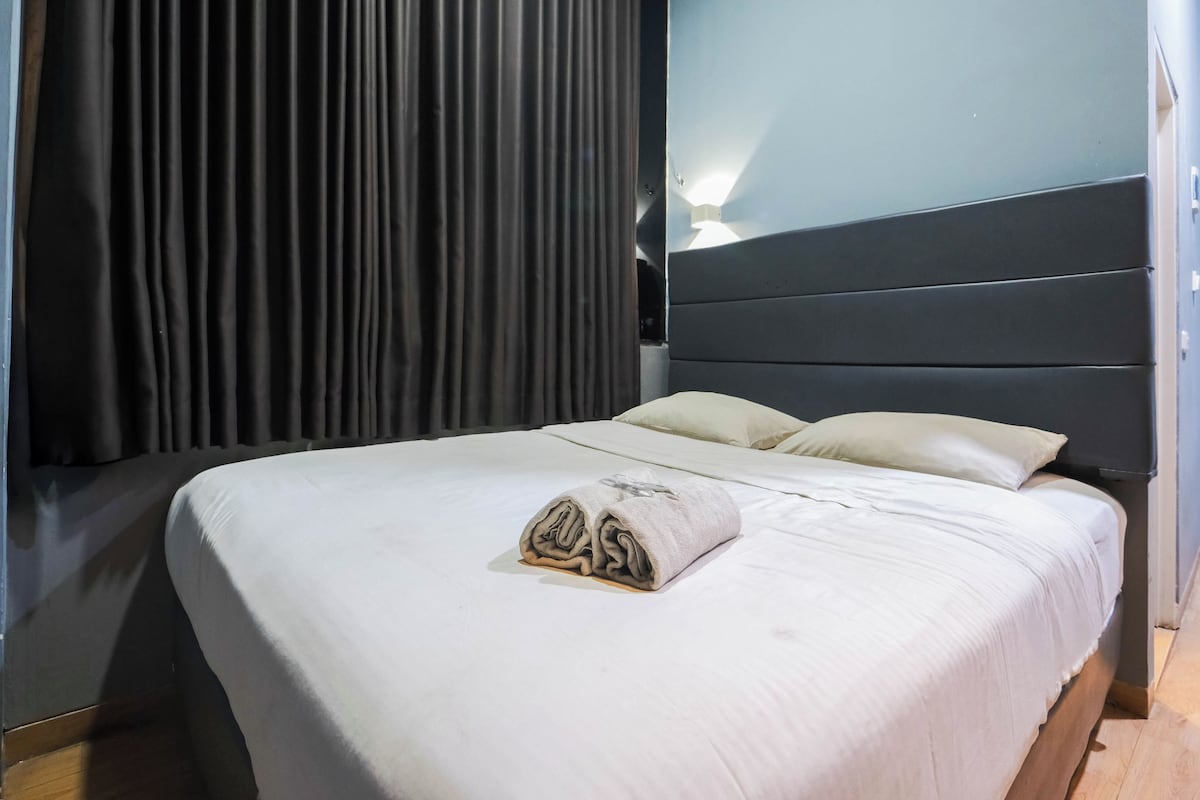 Een hotelkamer met een bed, donkere gordijnen, een hoofdeinde en een wandlamp.