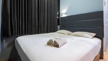 A hotel room with a bed, dark curtains, a headboard, and a wall-mounted light.