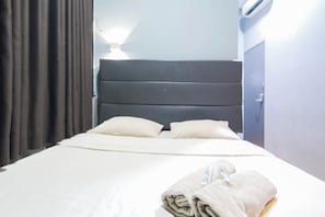 Een hotelkamer met een bed, nachtkastje, lamp en een raam met gordijnen.