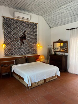 A bedroom with a bed, bedside tables, a wall-mounted air conditioner, a patterned tapestry, a mirror, and a window with curtains. - Mil Flores Pool Villa · Quinta de Margoa (Fajarda)