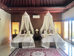 A double bed with a canopy, a nightstand with a lamp, and a large window with curtains. - Villa Sakura (Gianyar)
