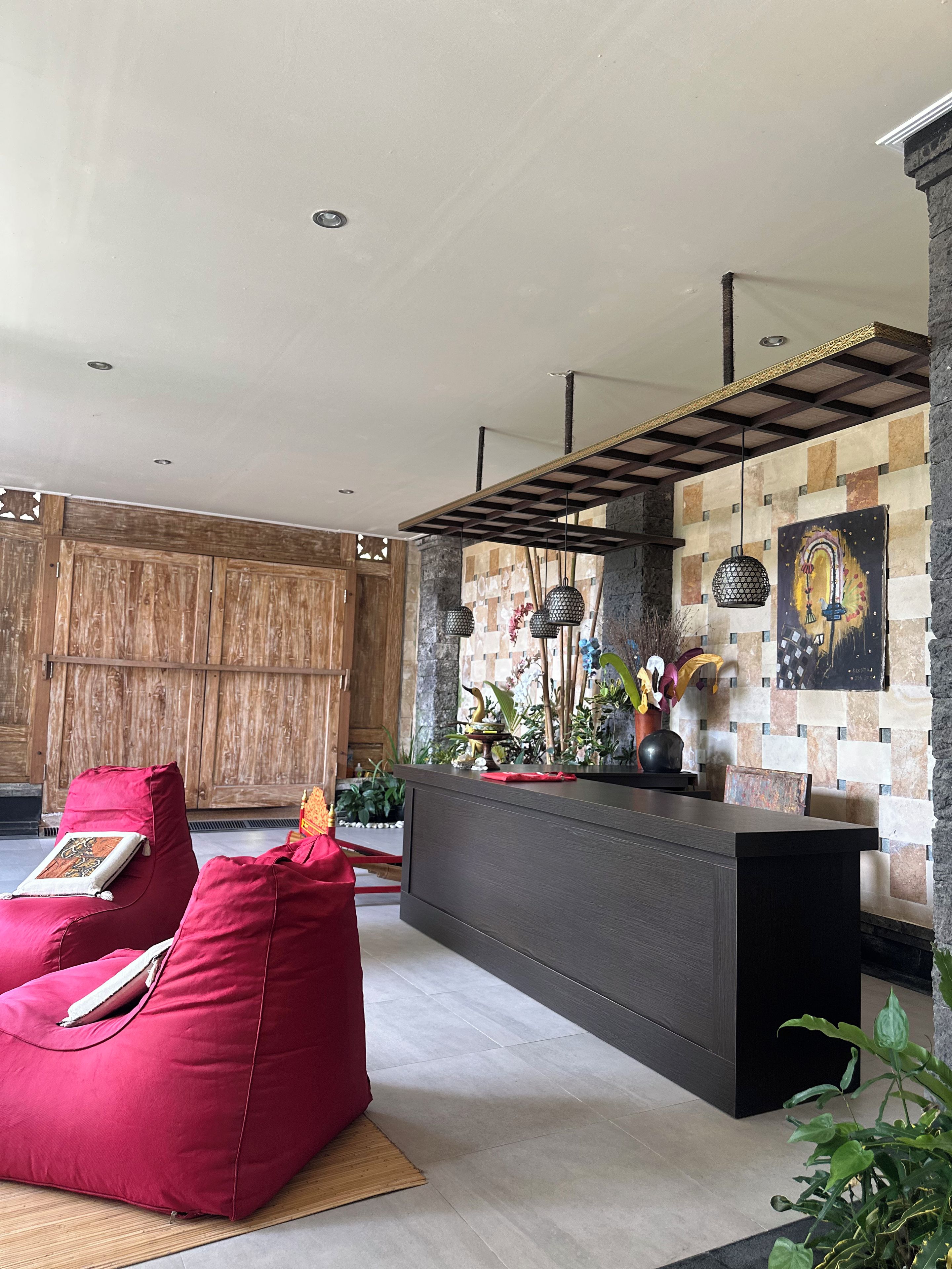 A modern interior with a wooden wall, a red sofa, a dark reception desk, and hanging pendant lights.