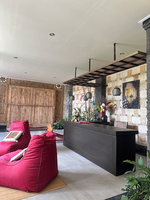 A modern interior with a wooden wall, a red sofa, a dark reception desk, and hanging pendant lights. - Villa Sakura (Gianyar)