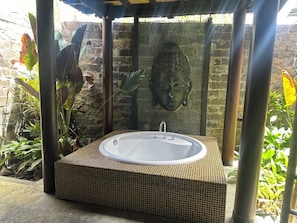 A hot tub in a covered outdoor area with a stone wall and plants. - Villa Sakura (Gianyar)