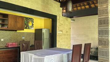 An outdoor dining area with a table and chairs, a ceiling fan, and a kitchen area with a refrigerator.