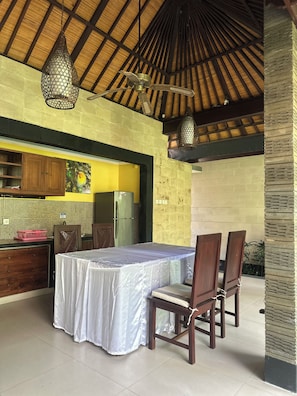 An outdoor dining area with a table and chairs, a ceiling fan, and a kitchen area with a refrigerator. - Villa Sakura (Gianyar)