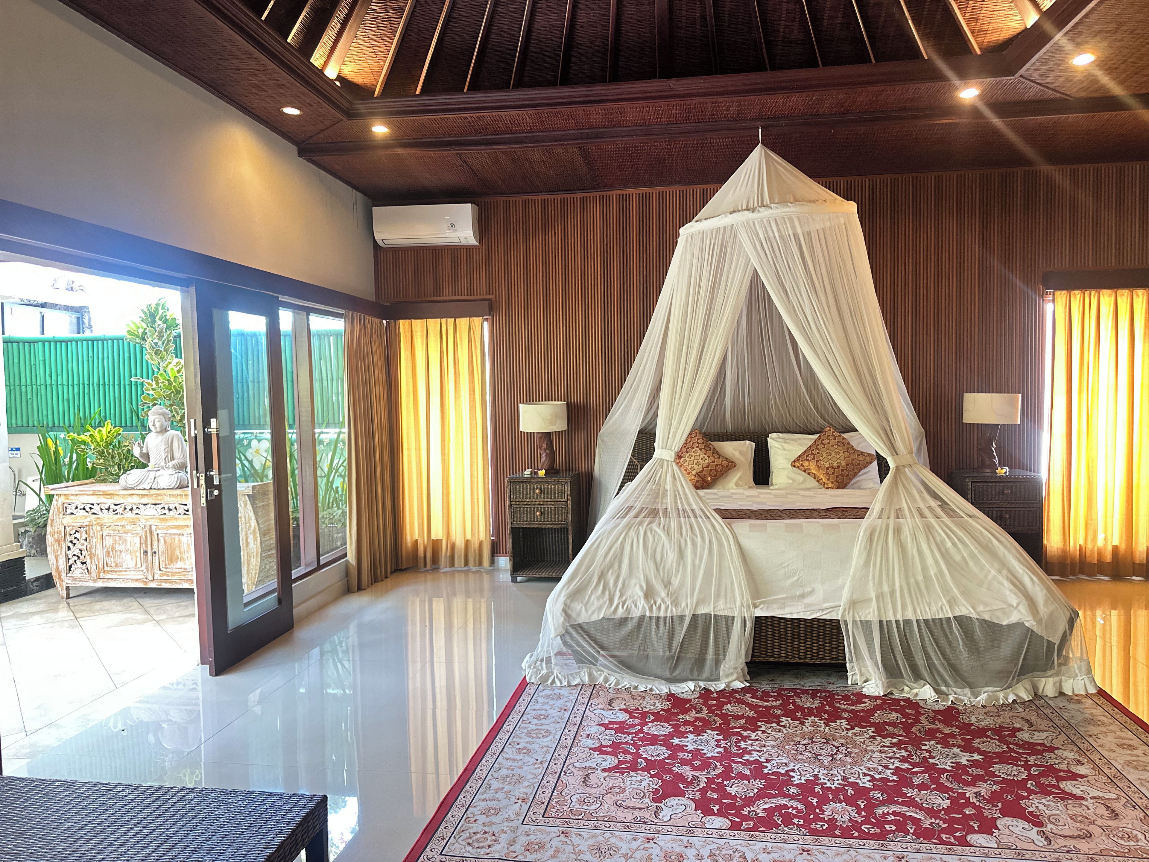 A bedroom with a canopy bed, a large window, and a view of greenery outside.