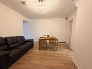En stue med en sort lædersofa, et træspisebord med fire stole og en loftlampe.
