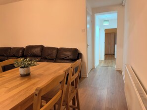 Spiseområde med et træbord og stole, en brun lædersofa og en potteplante.