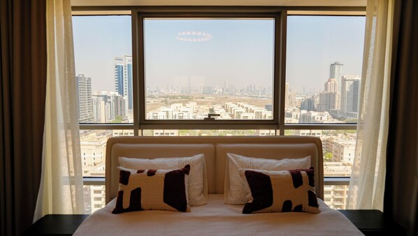 A hotel room with a large window, two beds with patterned pillows, and a view of a cityscape.