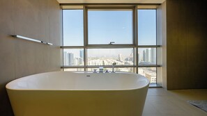 A modern bathroom with a freestanding bathtub, large windows, and a city view.