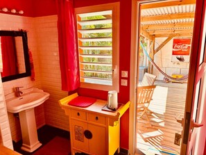 Une petite salle de bain avec un lavabo, une fenêtre avec des stores et un rideau rouge.