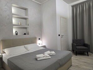 Una habitación de hotel con cama, mesitas de noche, una silla, una puerta y una ventana con cortinas.