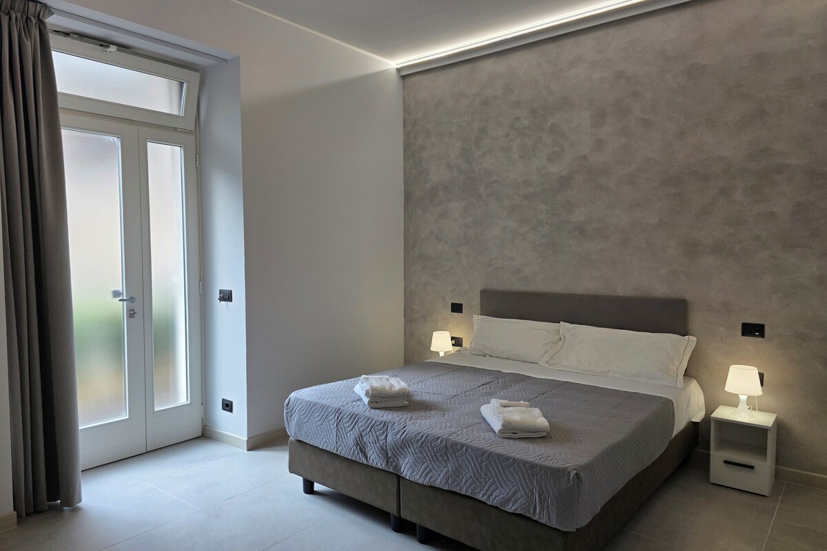 Un dormitorio moderno con cama, lámparas de noche y vistas a través de una puerta.
