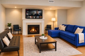 A living room with a fireplace, a blue sofa, a black leather couch, and a flat-screen TV displaying a Netflix show. - Downtown Suite - Spacious! RnRHoF, Casino, Stadium (Cleveland)