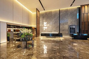Eine moderne Lobby mit Marmorboden, einem Empfangstresen und einem an der Wand befestigten Fernseher.