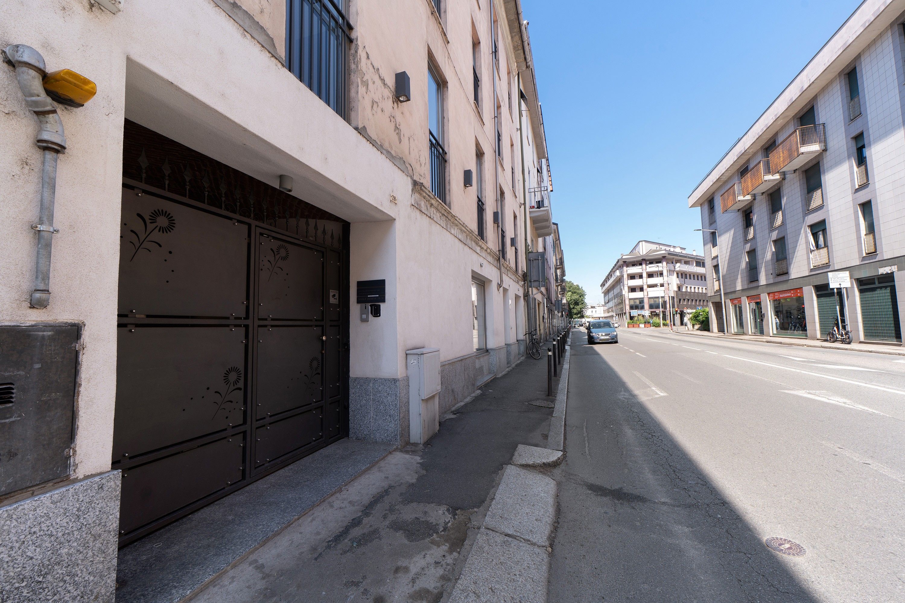 Straßenansicht mit einem Gebäude, das ein großes schwarzes Tor, einen Bürgersteig und einen strahlend blauen Himmel zeigt.