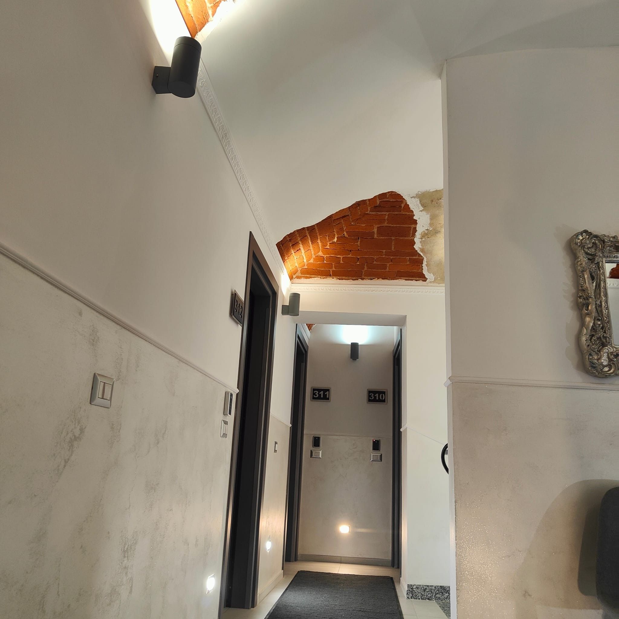 Un couloir avec un mur en briques, une porte et un tableau encadré accroché au mur.