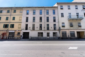 Une rangée d’immeubles à plusieurs étages dotés de balcons, une rue devant, et un ciel dégagé.
