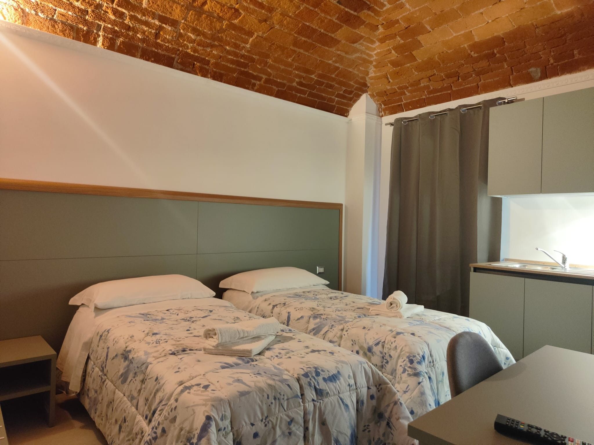 Une chambre d’hôtel avec un plafond en briques, un lit recouvert d’une literie à motifs floraux, un petit bureau et une fenêtre avec des rideaux.