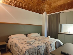 Une chambre d’hôtel avec un plafond en briques, un lit recouvert d’une literie à motifs floraux, un petit bureau et une fenêtre avec des rideaux.