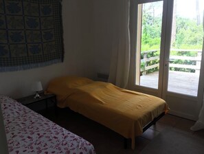 A room with a bed, a bedside table, a lamp, and a view of a wooden deck through a glass door. - New Listing (Moliets-et-Maa)
