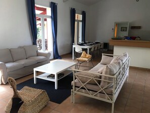 Ein Wohnzimmer mit einer Couch, einem Couchtisch, einem Korbstuhl und einem Essbereich mit Stühlen und einem Tisch.