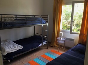 Ein Schlafsaalzimmer mit Etagenbetten, einem kleinen Tisch mit Lampe und Blick auf Grün durch ein Fenster.