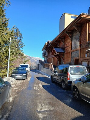 Eine Straße mit parkenden Autos, ein Gebäude mit Holzfassade und ein Berg im Hintergrund.