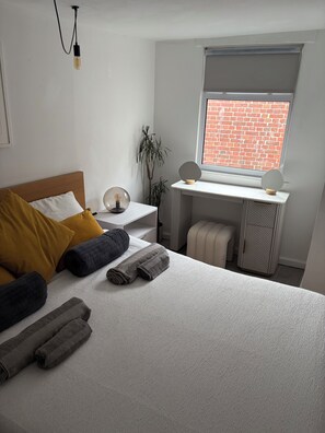 Un dormitorio moderno con cama, mesita de noche, escritorio y ventana con vistas a un muro de ladrillo.