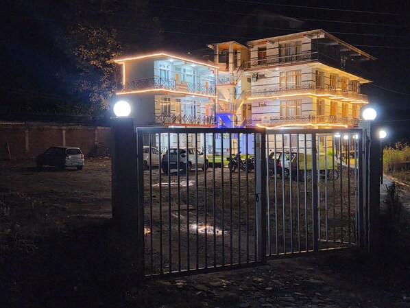 A gated residential building at night with multiple levels and balconies, surrounded by parked cars. - Solang Valley Homestay (Manali)
