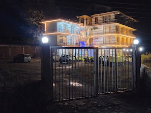 Un edificio residencial con acceso restringido, de varios niveles y balcones, rodeado de automóviles estacionados, visible de noche.
