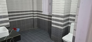 A bathroom with striped tile walls, a black floor, a white toilet, and a small sink with a red bucket. - Solang Valley Homestay (Manali)