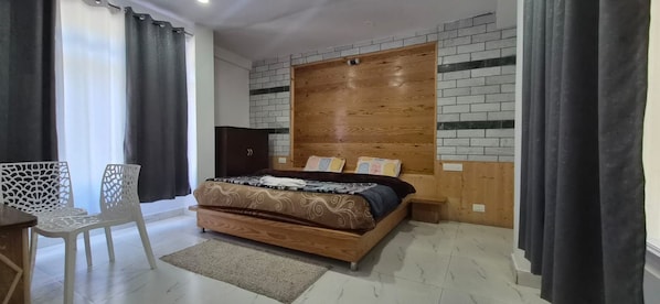 Un dormitorio con una cama, cabecera de madera, una silla blanca y una mesita.