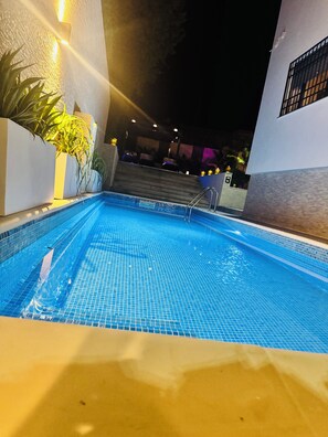 Piscina com degraus de acesso, cercada por paredes e plantas em vasos.