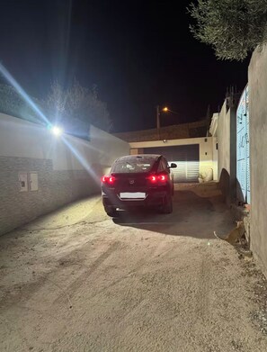 Une voiture était garée dans une ruelle faiblement éclairée, avec un immeuble d’un côté et un mur de l’autre.