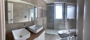 Un bagno moderno con due lavabi, cabina doccia e uno specchio grande.