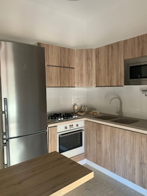 Eine kleine Küche mit einem Edelstahl-Kühlschrank, einem Gasherd und Holzschränken.