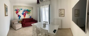 Un soggiorno con un divano rosso, un tavolo da pranzo bianco e una grande mappa astratta del mondo appesa al muro.
