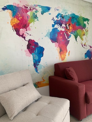 Ein Zimmer mit einer farbenfrohen Weltkarte an der Wand, einem grauen Sofa mit zwei Kissen und einem roten Sessel.