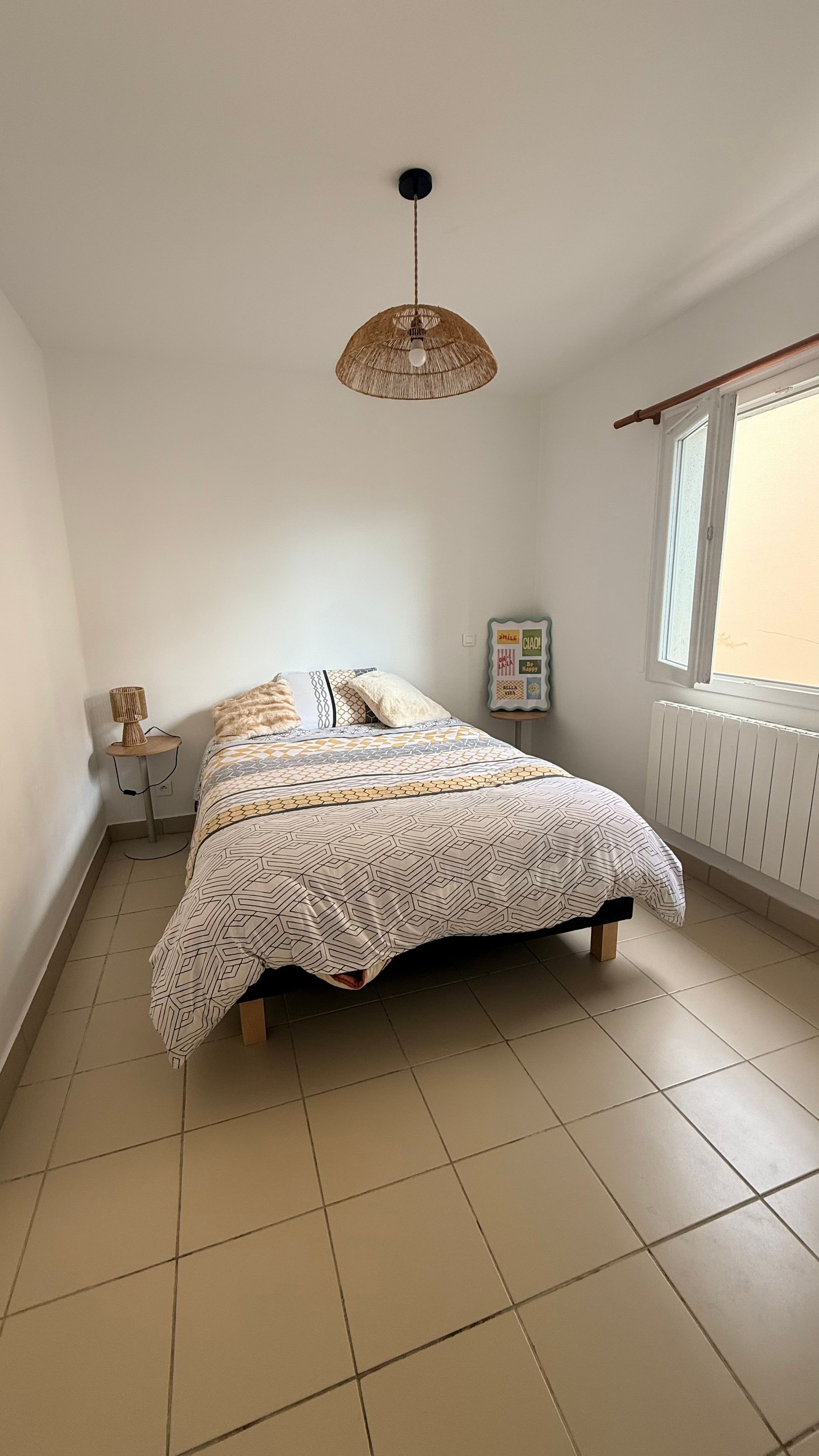 Un dormitorio con una cama, una lámpara colgante, una mesita con lámpara y un ventanal con vistas.